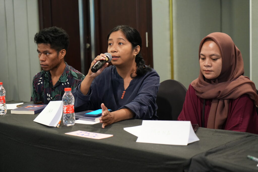 A woman speaking into a microphone while sitting at a table.