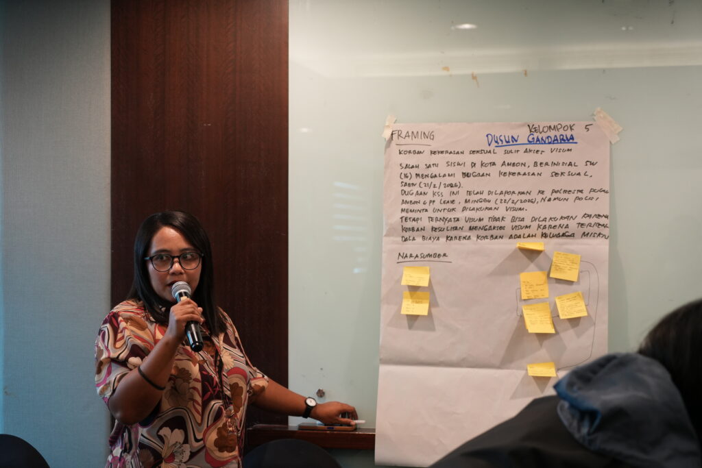 A woman speaking into a microphone while referring to a poster.